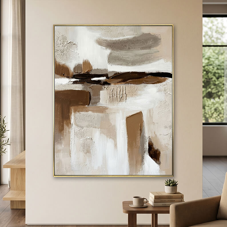 Minimalist beige and dark brown 3D textured canvas art displayed on a neutral wall above a small wooden table with books.
