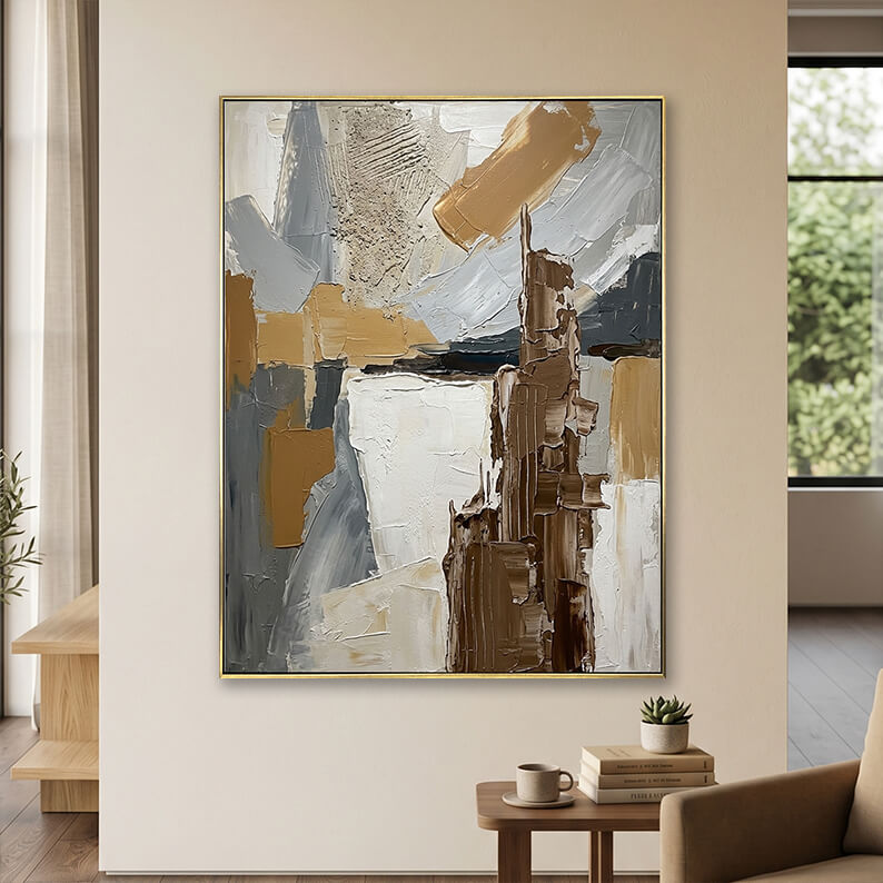 Minimalist beige grey and brown 3D textured canvas art displayed on a neutral wall above a small wooden table with books.