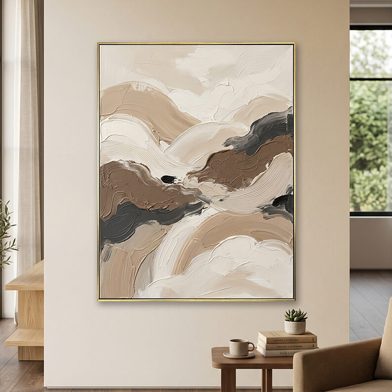 Minimalist beige grey and brown 3D textured canvas art displayed on a neutral wall above a small wooden table with books.