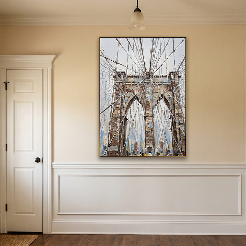 Detailed Description: An elegant hallway or entryway interior mock-up. The textured Brooklyn Bridge painting hangs centered on a warm beige wall. Below the painting is clean white wainscoting with decorative rectangular trim. To the left is a traditional white paneled interior door with a black doorknob and heavy molding. A single glass bowl pendant light hangs from the ceiling, casting a warm glow,