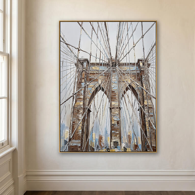 Framed abstract Brooklyn Bridge art hung next to a large white-framed window on a textured cream wall.
Detailed Description: A minimalist home interior. The vertical Brooklyn Bridge painting hangs in a thin gold frame on a flat, cream-colored plaster wall. To the left of the artwork is a classic white-trimmed sash window letting in bright, natural light. The floor is a dark-stained hardwood, and elegant white baseboard molding runs along the bottom of the wall.
Image 7: YX548-9 (7).jpg (Cozy Living Room /