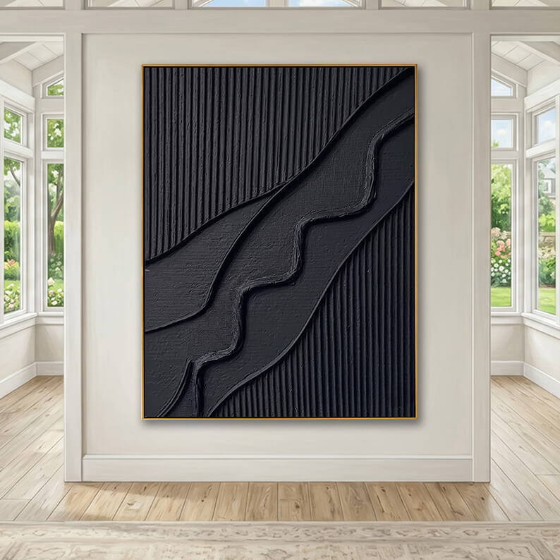 The large black textured artwork serves as a focal point, hung on a central cream-colored structural pillar or partition wall. The room is flooded with natural light from large multi-pane, white-trimmed windows on either side that look out onto a lush green garden. The space is completely minimalist and empty, featuring polished light wood floors, which emphasize the artwork's grand scale and sculptural texture.