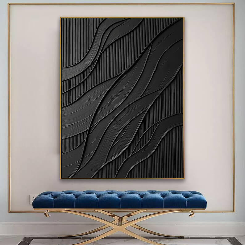 The textured black canvas artwork showcased inside a larger, gold-trimmed decorative wall recess on a white wall. Below the painting is a luxurious, long bench upholstered in deep blue tufted velvet, supported by an elegant, curved gold metal cross-leg frame.