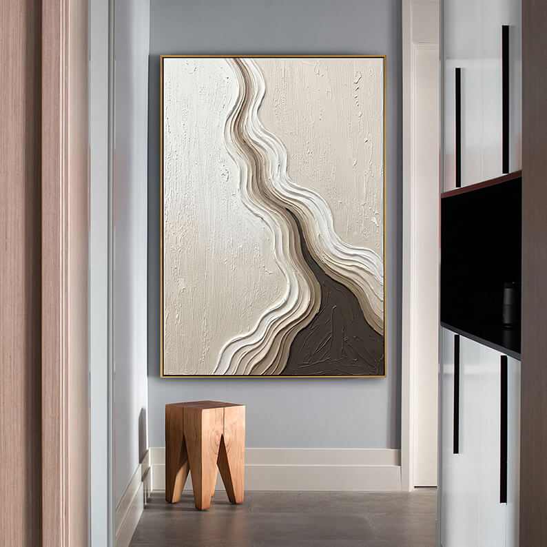 Modern earthy tone textured wall art hung on a cool grey wall beside a contemporary wooden stool in a minimalist interior space.