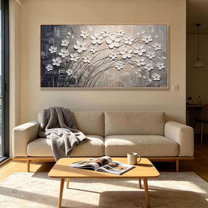 Horizontal hand-painted white cherry blossom painting with rich 3D texture hanging above a beige couch in a minimalist living room.