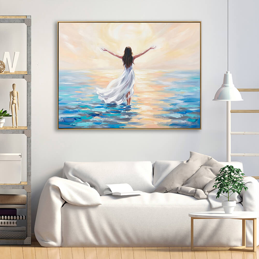 Uplifting hand-painted sunrise woman seascape canvas displayed above cream linen sofa in bright neutral living room