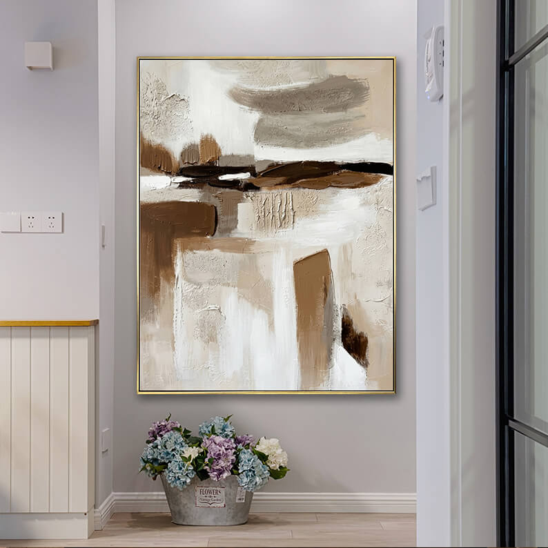 Neutral wabi-sabi style textured abstract canvas art hanging in a bright home corridor next to a bucket of flowers.