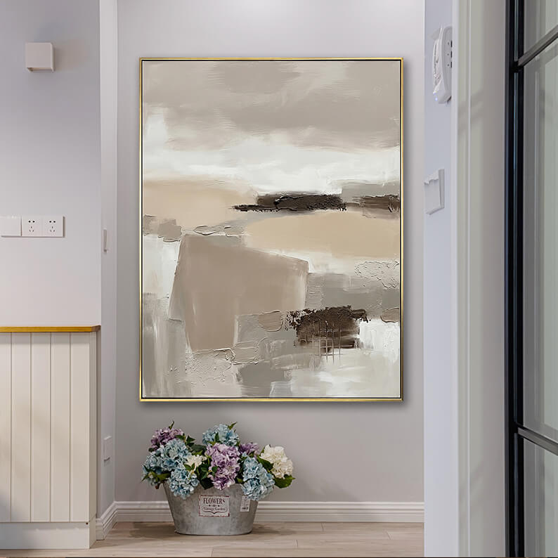 Neutral wabi-sabi style textured abstract canvas art hanging in a bright home corridor next to a bucket of flowers.