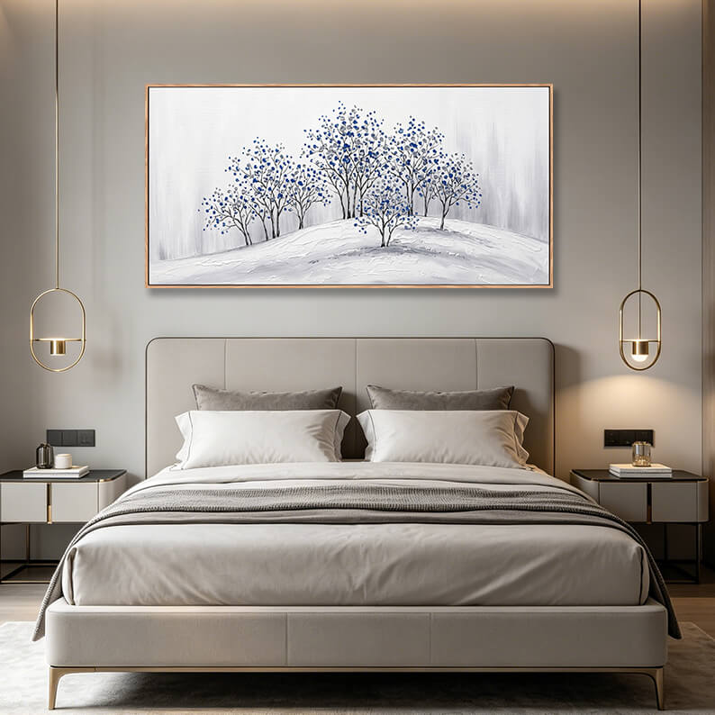 Panoramic horizontal blue and grey winter tree painting hanging over a grey upholstered bed in a luxury master bedroom.