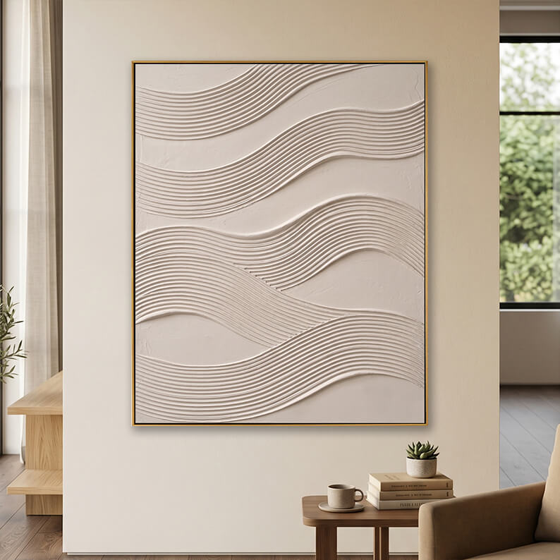 Minimalist beige 3D textured canvas art displayed on a neutral wall above a small wooden table with books.