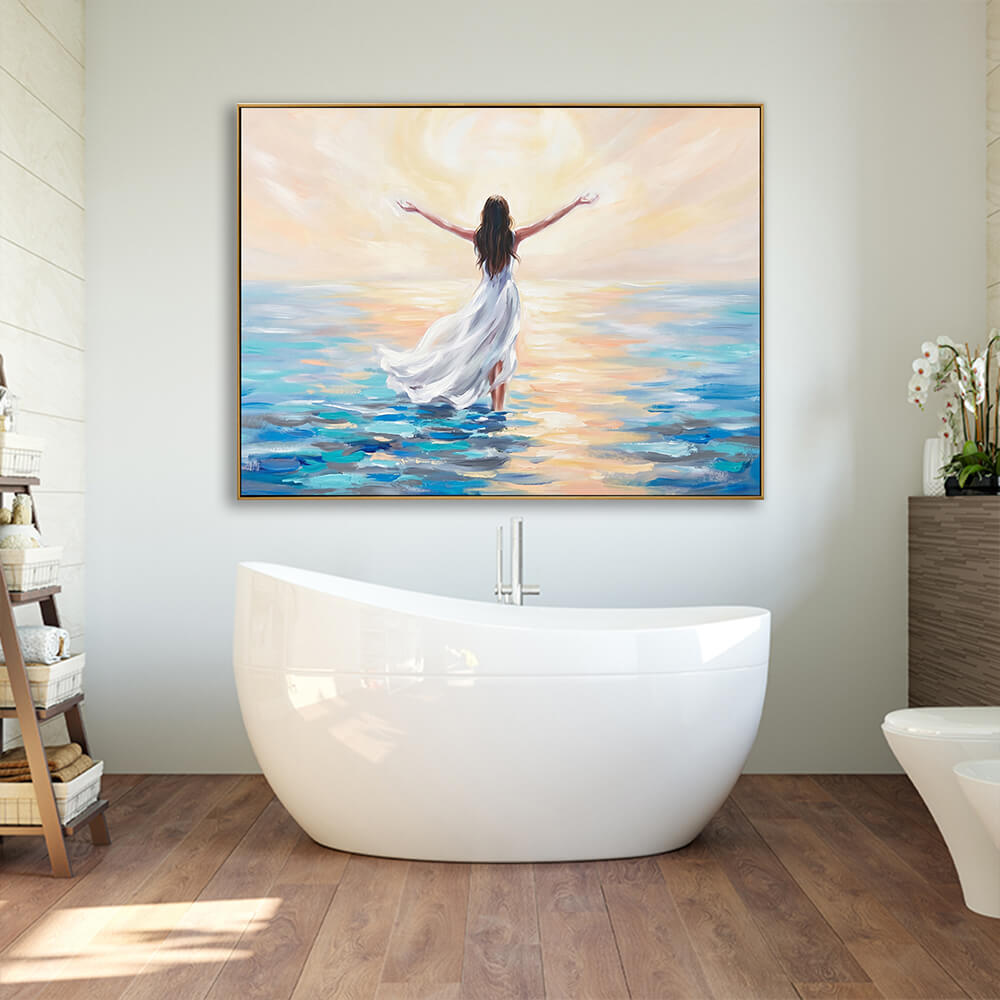 Hand-painted sunrise ocean woman canvas wall art hung above freestanding white bathtub, warm wood bathroom flooring