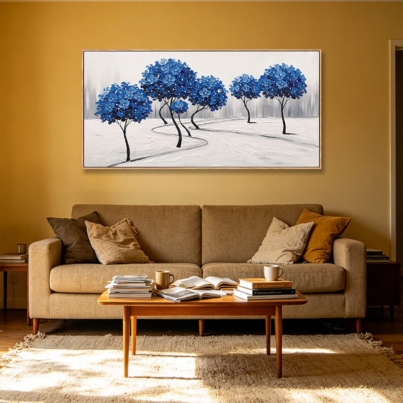 Panoramic horizontal blue and white tree landscape painting styled over a tan sofa in a living room with golden-yellow walls.