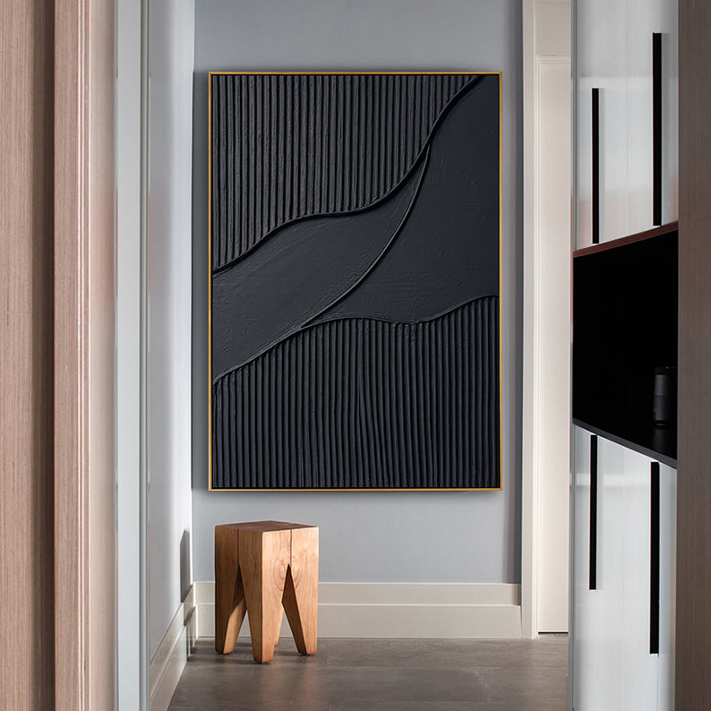 Vertical black 3D wall art hanging in a bright hallway next to a natural wooden stool.