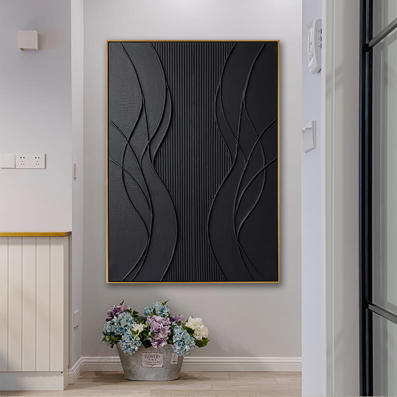 The modern black textured canvas painting is displayed on a light grey wall in a bright hallway. To the left is a white wainscoted wooden partition wall. Resting on the light wood floor directly beneath the painting is a rustic vintage-style metal bucket filled with a large, colorful bouquet of blue, purple, and white hydrangea flowers, creating a fresh, welcoming entryway scene.