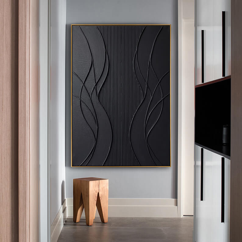 The black textured abstract painting is showcased on a minimalist grey wall. Directly below the gold-framed artwork sits a rustic, solid wood block stool on polished grey tiled flooring. To the left and right, clean architectural lines and light-colored wooden doors frame the corridor, highlighting a Scandinavian or Japandi-style interior design.