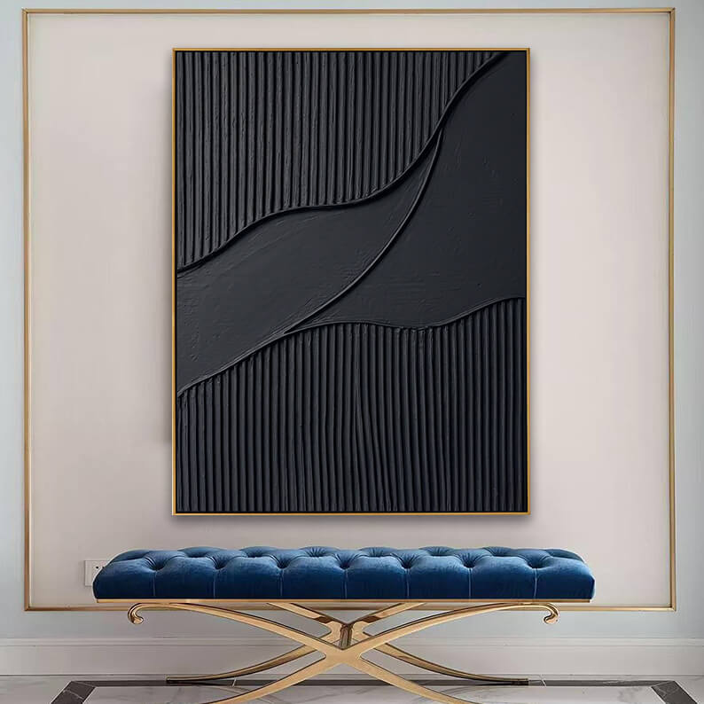 An elegant, luxurious interior scene. The black textured artwork is mounted inside a decorative, large gold-outlined wall molding frame on a light beige wall. Beneath the painting is a luxurious, long bench upholstered in royal blue tufted velvet with a polished criss-cross gold metal base. The floor features dark marble trim borders.