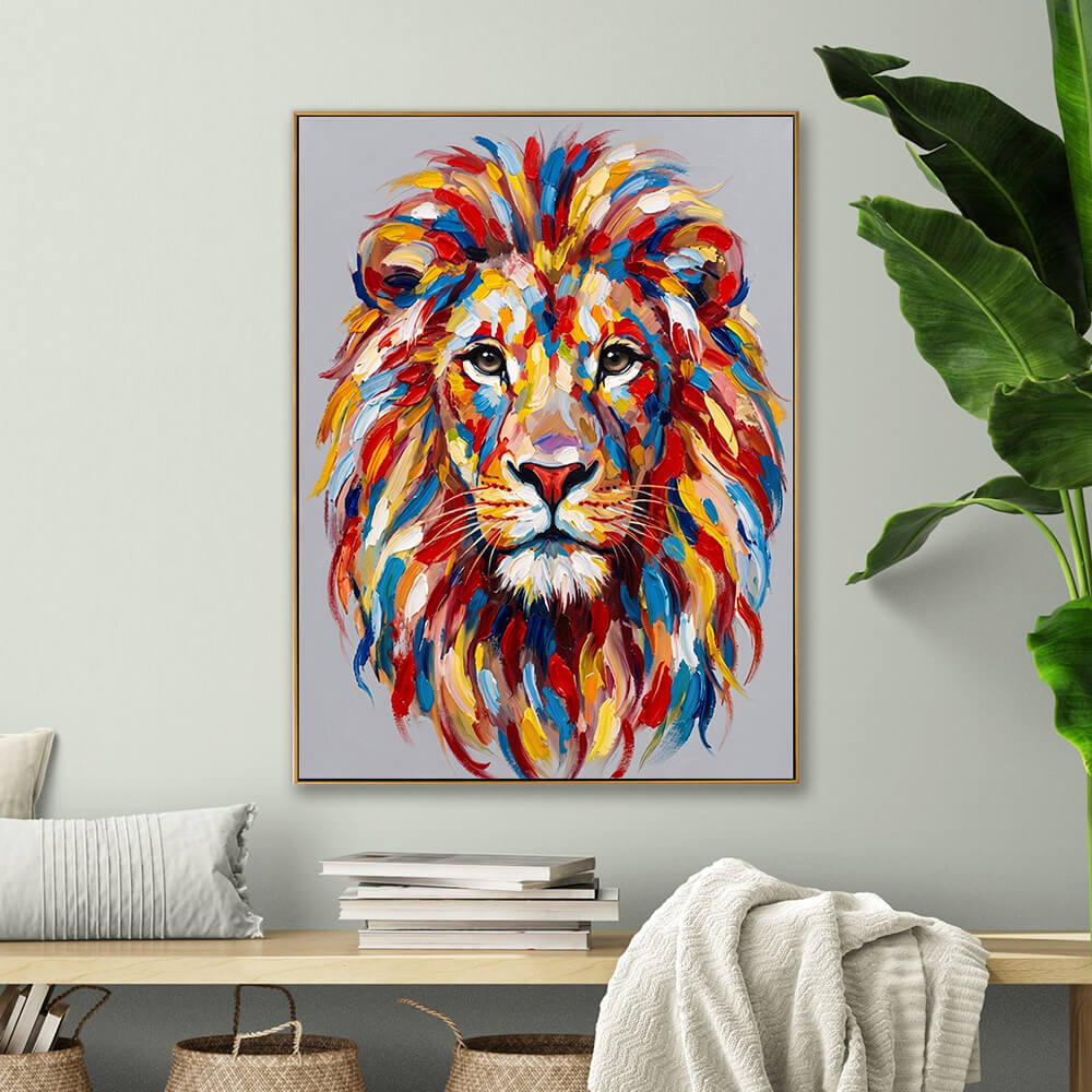 Cozy home decor mockup featuring a colorful textured lion canvas painting on a soft sage green wall. Below the artwork is a light wood console table with stacked books, a knit throw blanket, and a large potted banana leaf plant.