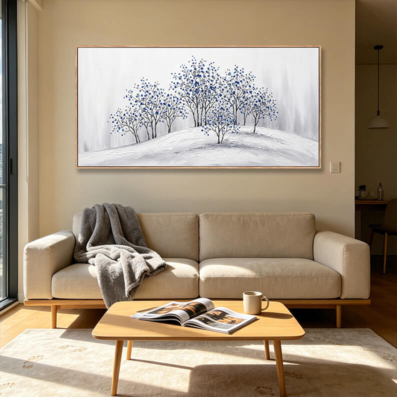 Horizontal hand-painted blue forest landscape painting showing impasto snow textures styled in a minimalist beige living room.