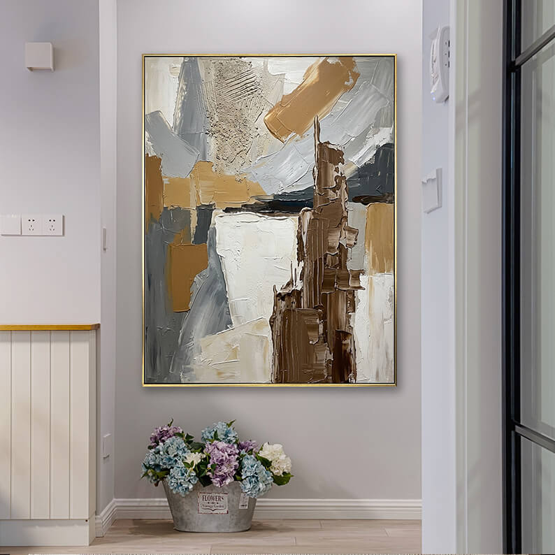 Neutral wabi-sabi style textured abstract canvas art hanging in a bright home corridor next to a bucket of flowers.