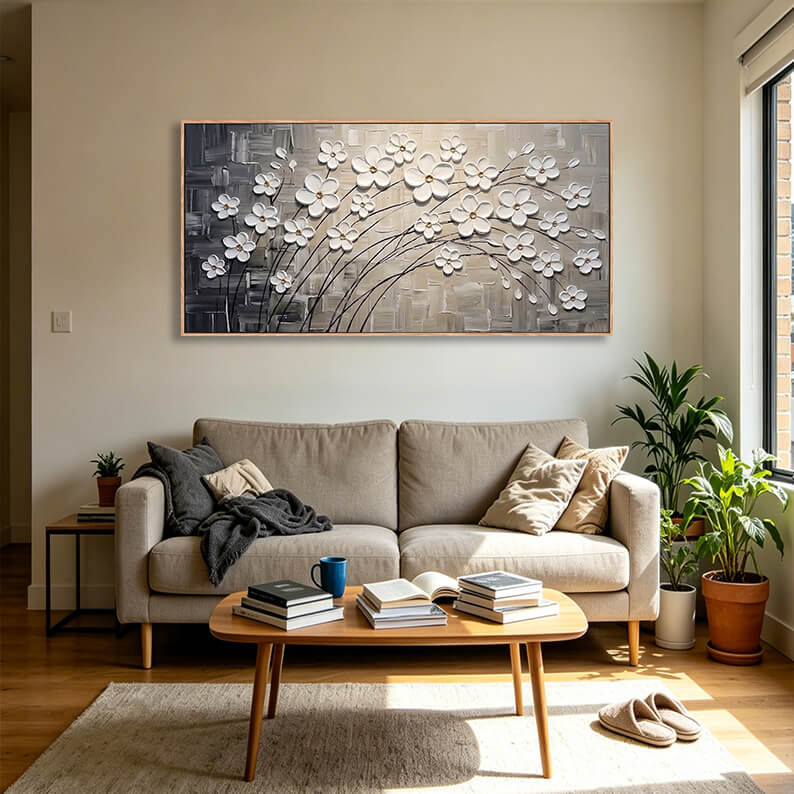 Large horizontal white cherry blossom canvas art hanging above a beige fabric sofa in a bright, modern sunlit living room.