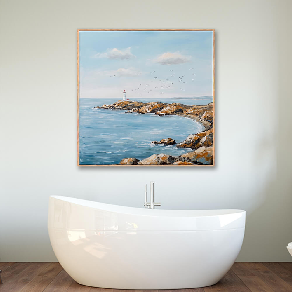 Framed rocky cove lighthouse seascape wall art hung above modern freestanding bathtub