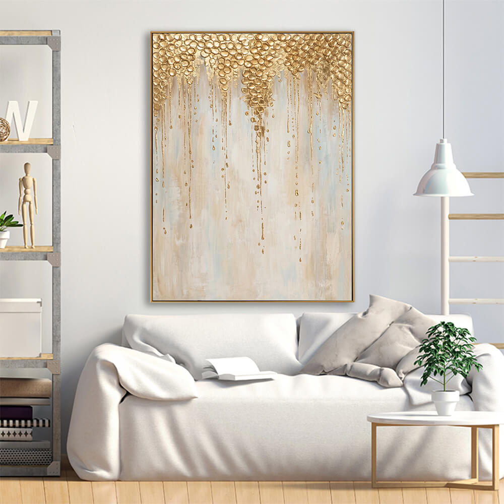 Hand-painted metallic gold leaf drip abstract canvas displayed above cream linen sofa in bright neutral luxury living room