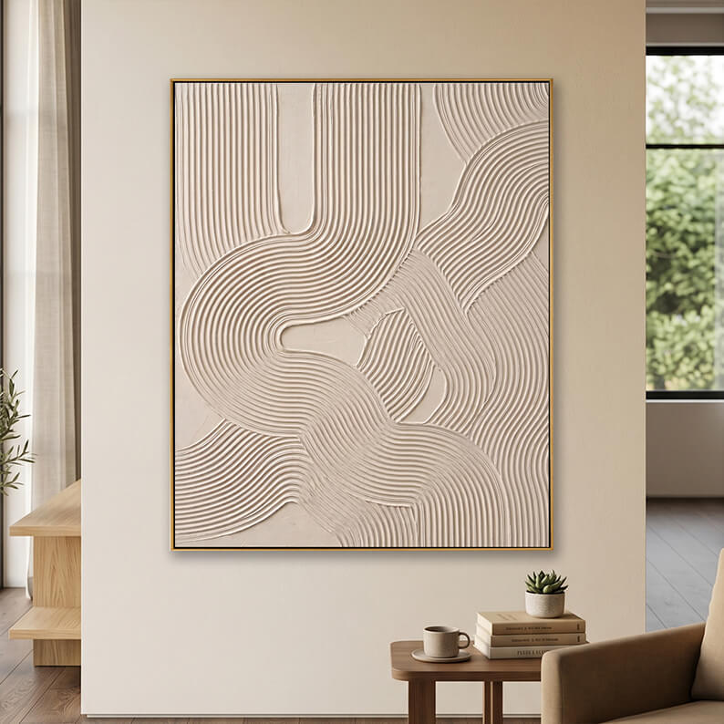 Minimalist beige 3D textured canvas art displayed on a neutral wall above a small wooden table with books.