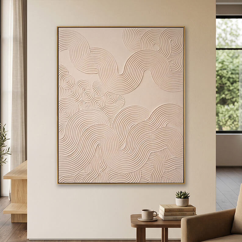 Minimalist beige 3D textured canvas art displayed on a neutral wall above a small wooden table with books.