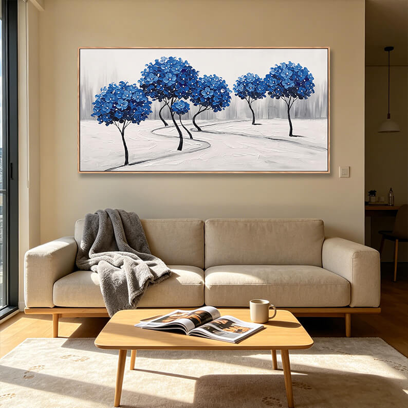 Horizontal hand-painted blue forest landscape painting with rich 3D texture hanging above a beige couch in a minimalist living room.