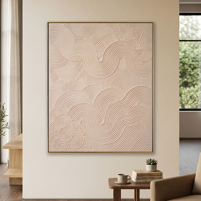 Minimalist beige 3D textured canvas art displayed on a neutral wall above a small wooden table with books.