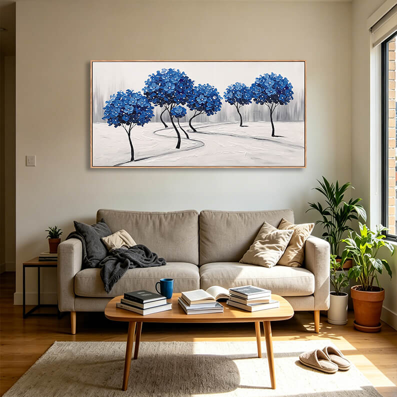 Large horizontal blue tree forest canvas art hanging above a light grey fabric sofa in a bright, modern contemporary living room.