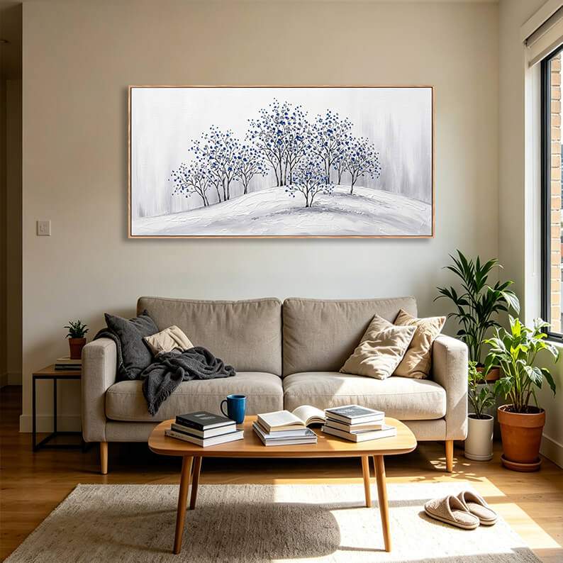 Large horizontal blue blossom forest canvas art styled in a bright minimalist living room above a contemporary grey fabric sofa.