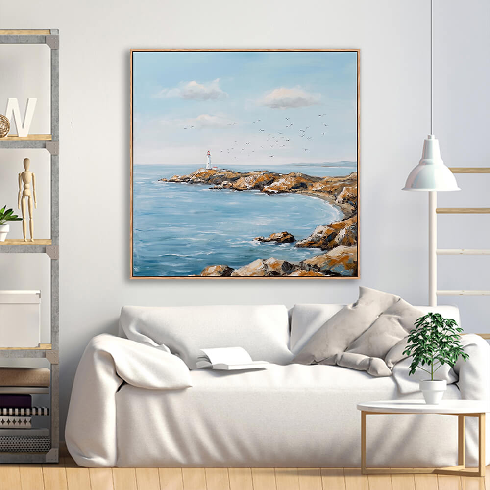 Tranquil rocky coastline lighthouse seascape painting above cream linen minimalist sofa