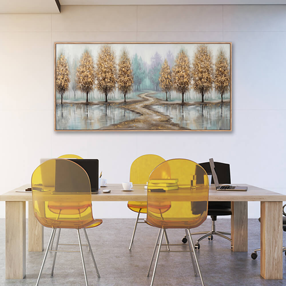 Wide golden tree landscape painting hanging above a light wood table with yellow translucent chairs in a bright, modern office space.