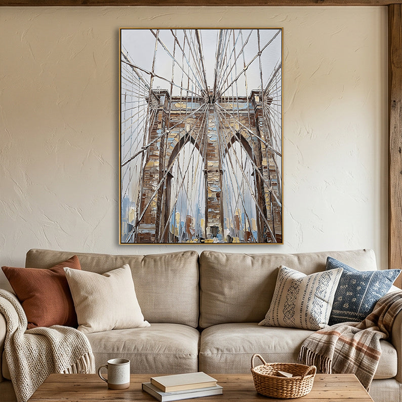 Hand-painted Brooklyn Bridge cables art in sepia and ochre above a beige sofa in a cozy living room.